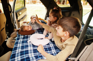 Family of four kids at vehicle interior. Children in trunk. Traveling by car, lying and having fun, atmosphere concept.