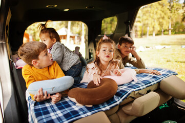 Family of four kids at vehicle interior. Children in trunk. Traveling by car, lying and having fun, atmosphere concept.