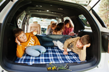 Mother with four kids at vehicle interior. Children in trunk. Traveling by car, lying and having fun, atmosphere concept.