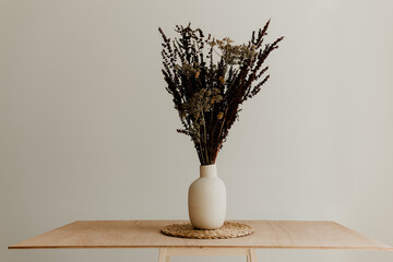 A bunch of wild dried flower in white ceramic vase closeup on brown wooden table	