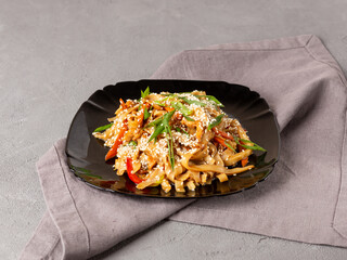 Asian vegetarian food udon noodles with mushrooms, sesame and pepper close-up on a black plate. Grey Napkin