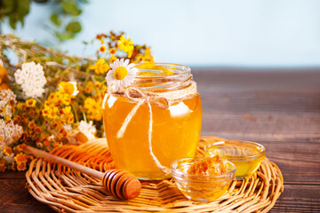 Sweet and flavored honey in jar and honeycomb in small bowl. Bouquet of wild flowers on the...