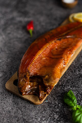 Whole smoked trout on a wooden board on a dark background