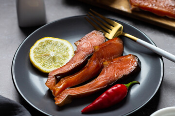 Pieces of smoked trout on a gray plate on a dark background. Snack. close-up. Restaurant serving