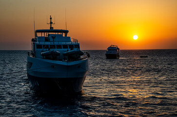 Two yachts mooring in a reef with calm sea an orange sky at sunset