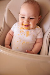 Cheerful baby boy playing in high chair after meal