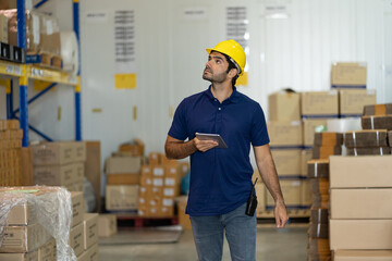 Warehouse male worker using digital ipad for work in the warehouse near shelf pallet of products or parcel goods.