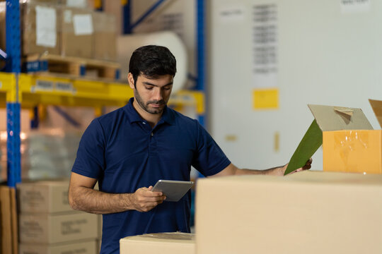 Warehouse Male Worker Working With Digital Ipad For Work In The Warehouse Near Shelf Pallet Of Products Or Parcel Goods.