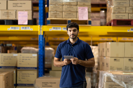 Portrait of warehouse male worker using digital ipad for work in the warehouse near shelf pallet of products or parcel goods.