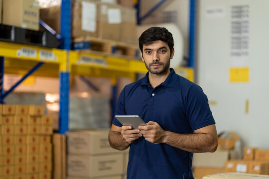 Warehouse Male Worker Using Digital Ipad For Work In The Warehouse Near Shelf Pallet Of Products Or Parcel Goods.