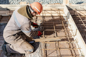 A worker uses steel tying wire to fasten steel rods to reinforcement bars. Reinforced concrete structures - knitting of a metal reinforcing cage. Preparation for concreting the foundation.