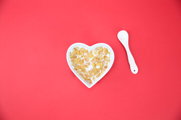 cornflakes in heart shaped bowl on red background