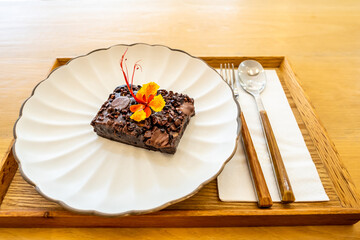 Homemade brownies with chocolate chip on a white plate, spoon and fork on a wooden background.