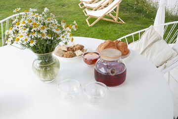 Fresh sweet croissants on the table with tea and a vase of daisies. Sunday breakfast in the backyard of the cottage. High quality photo