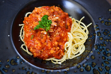 Delicious spaghetti with meat, tomato sauce served on a black plate.