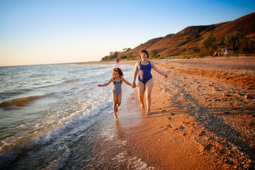 Sister girls in swimsuits run and play on the seashore, free summer vacation and happy children