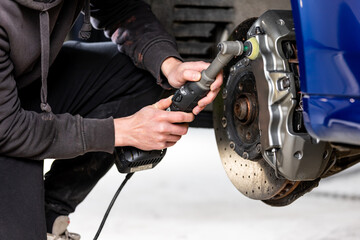 Fototapeta premium Car detailing - Hand with orbital polisher in auto repair shop, polishing modern car brakes