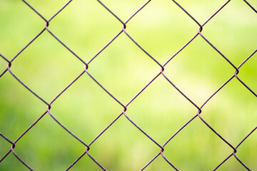 Mesh cage in the garden with green grass as background. Metal fence with wire mesh. Blurred view of the countryside through a steel iron mesh metal fence on green grass. Abstract background.