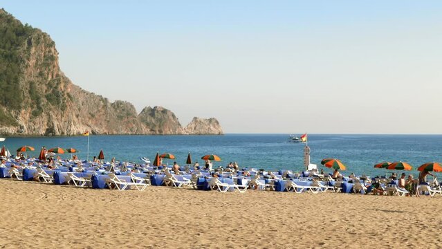 View of Cleopatra beach with tourists and sunbeds. People rest and have sunbathe on beautiful beach with mountain on background. 