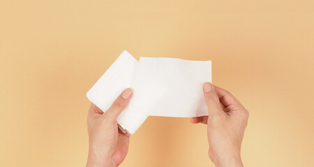 The hand is holding a small size of white paper tissues on a creamy ivory color background.