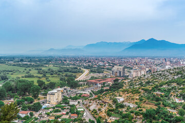 Shkoder, Albania - June 21, 2021: Top view of the highway to Shkoder and the city on the horizon against the backdrop of mountains, Albania. Beautiful Albanian urban-natural panorama on a summer day