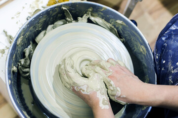 Top view of female pottery artist hands molding clay on pottery wheel at ceramic art workshop.