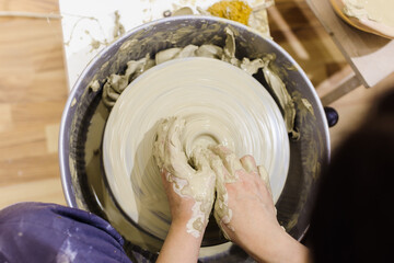 Fototapeta premium Top view of female pottery artist hands molding clay on pottery wheel at ceramic art workshop.