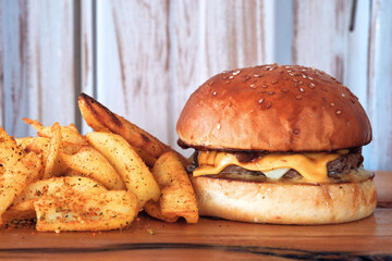 One hamburger, burger, or cheeseburger on wooden plate with French fries potato chips.