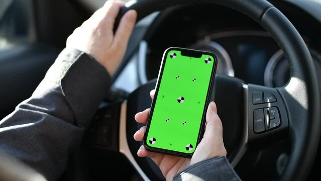 Closeup shot of smartphone with mockup green screen held by the female driver in car over the steering wheel