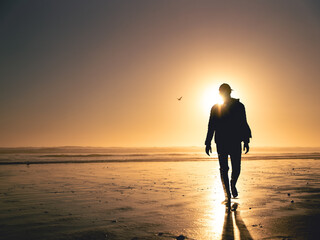 Silhouette of a man walking away from the sun on the beach