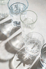 Glasses of water and sharp hursh shadows stands on abright background. Drinking water concept