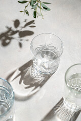 Glasses of water and sharp hursh shadows stands on abright background. Drinking water concept