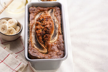 Chocolate banana bread with walnuts in a metallic baking mold and ingredients on a grey neutral...
