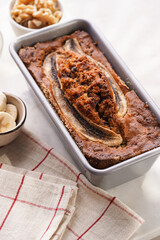 Chocolate banana bread with walnuts in a metallic baking mold and ingredients on a grey neutral background with creative lighting, top view