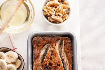 Chocolate banana bread with walnuts in a metallic baking mold and ingredients on a grey neutral background with creative lighting, top view