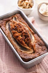 Chocolate banana bread with walnuts in a metallic baking mold and ingredients on a grey neutral background with creative lighting, top view