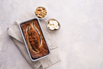 Chocolate banana bread with walnuts in a metallic baking mold on a grey neutral background, top view, space for text