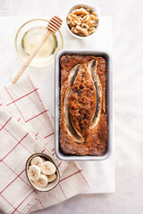 Chocolate banana bread with walnuts in a metallic baking mold on a grey neutral background with creative lighting, top view