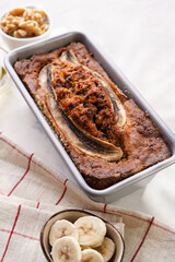 Chocolate banana bread with walnuts in a metallic baking mold on a grey neutral background with creative lighting