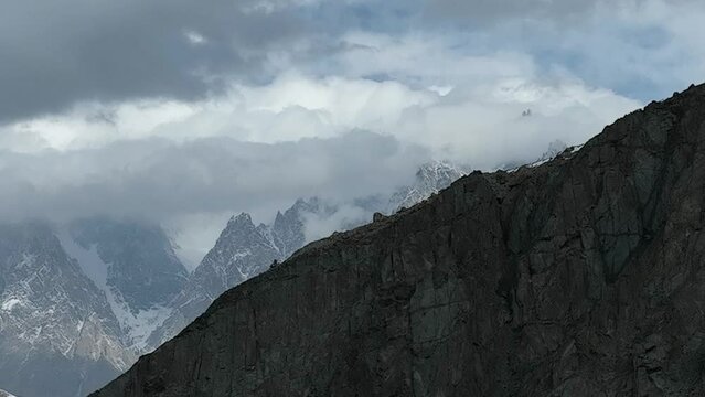 Aerial Rising Behind Mountain Wall To Reveal Passu Cones In the Karakoram Range Hiding In Clouds. Establishing Shot