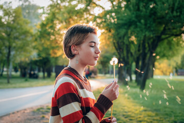 Teenage girl with short hair blowing on dandelion in the park