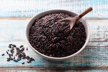 Black wild rice in a bowl. Blue wooden background. Close up.