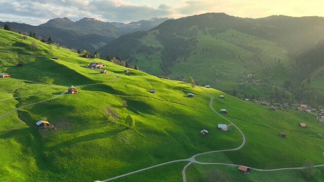 Swiss meadow with green rolling hills and mountains in the morning, idyllic rural landscape in Switzerland, aerial view of Swiss village