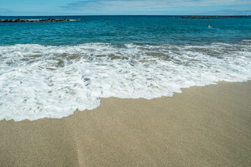 Ocean foam covering beautiful long sandy beach.