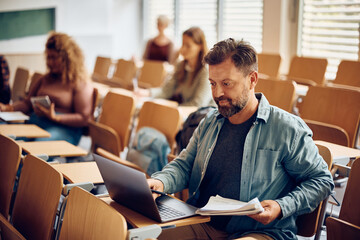 Mature man e-learning on laptop during lecture at university classroom.