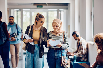 Happy Muslim student and her friend read their exam results while walking through university hallway.