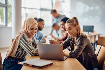 Happy female students using computer while e-learning in classroom at university.