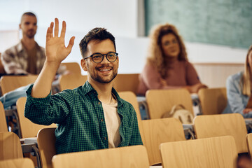 Happy college student raising his hand to ask question during class.