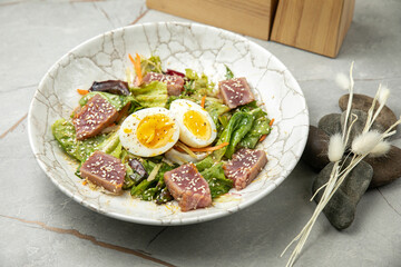salad with tuna, lettuce, herbs, egg, on a gray table
