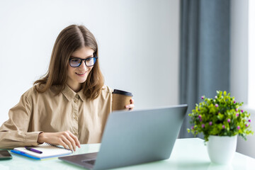 Cheerful caucasian businesswoman sitting in office and holding cup with coffee.